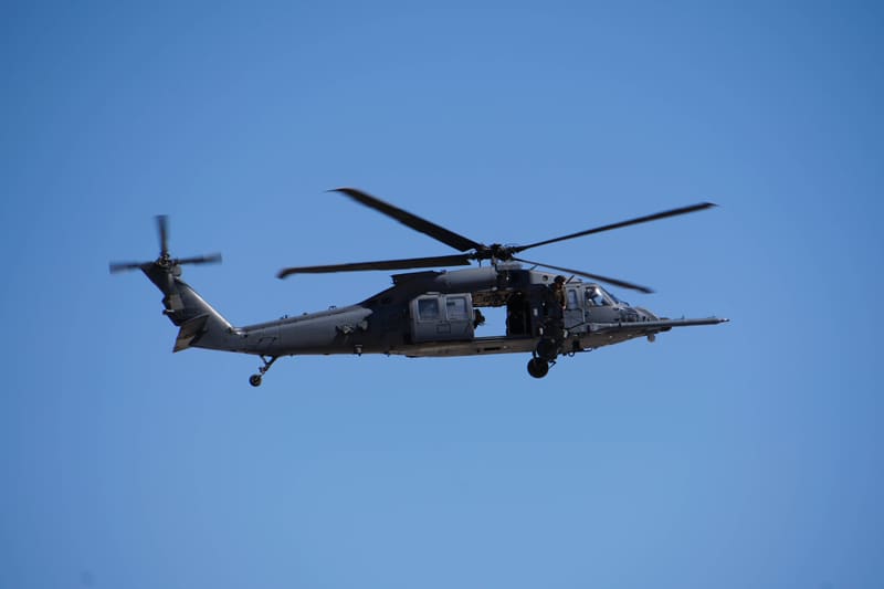 Grey HH-60 Pave Hawk helicopter in side profile against a clear blue sky, cabin door open and refuelling probe extended
