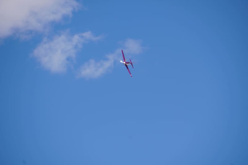 Magenta and white aerobatic monoplane banking hard against blue sky with wispy white clouds