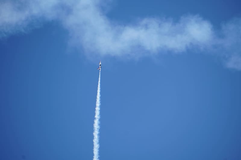 Lone USAF Thunderbirds F-16 climbing straight up on a single white smoke trail, wispy clouds across a blue sky