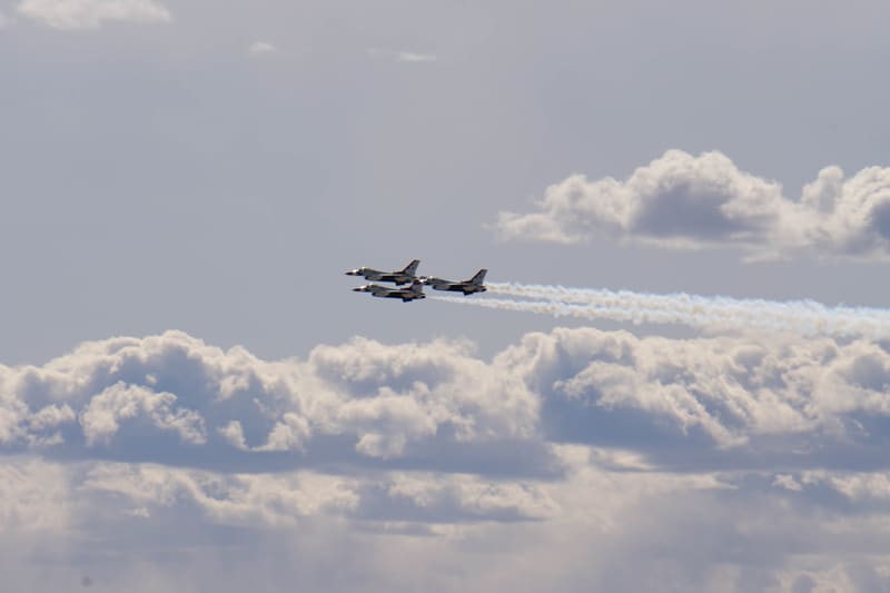 Three USAF Thunderbirds F-16s in close formation against a grey overcast sky, white smoke trailing behind them