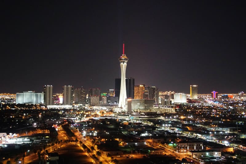 Las Vegas skyline at night with the Strat tower's red-lit spire rising above glowing Strip hotels and palm-lined streets