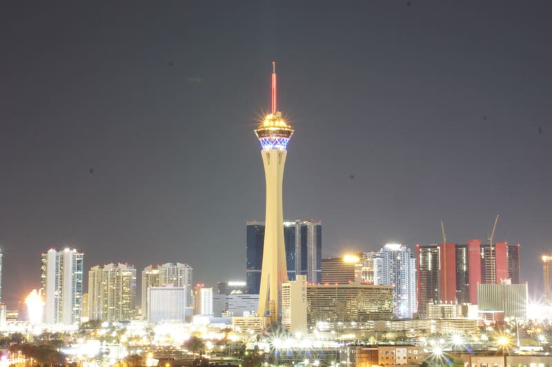 The Strat tower glowing gold at night above the Las Vegas skyline, red spire lit against a hazy grey sky