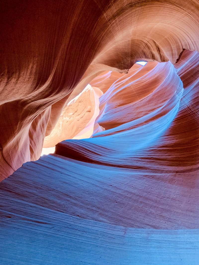 Looking up inside Antelope Canyon, blue-shadowed sandstone curling into glowing orange walls and a sliver of sky