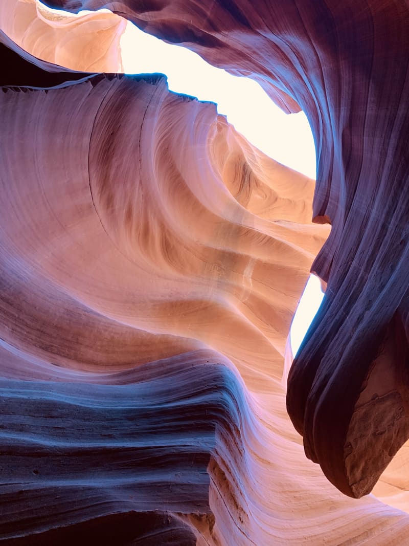 Swirling layered sandstone at Antelope Canyon, peach and pink bands curving under a dark overhang and white sky