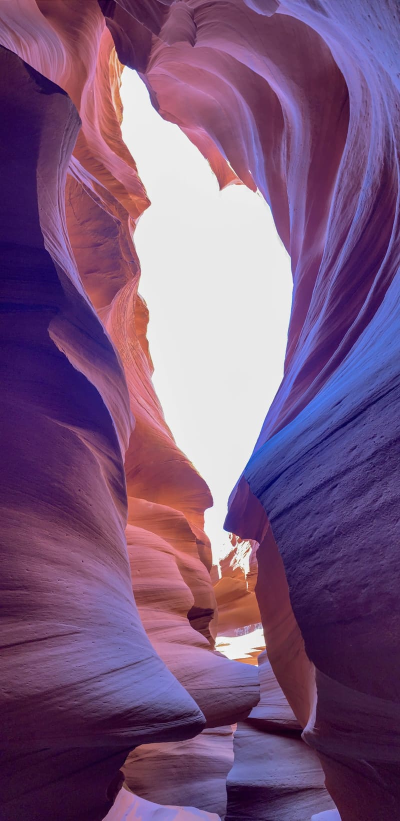 Tall narrow slot canyon passage at Antelope Canyon, purple-blue sandstone walls framing a bright white gap of sky