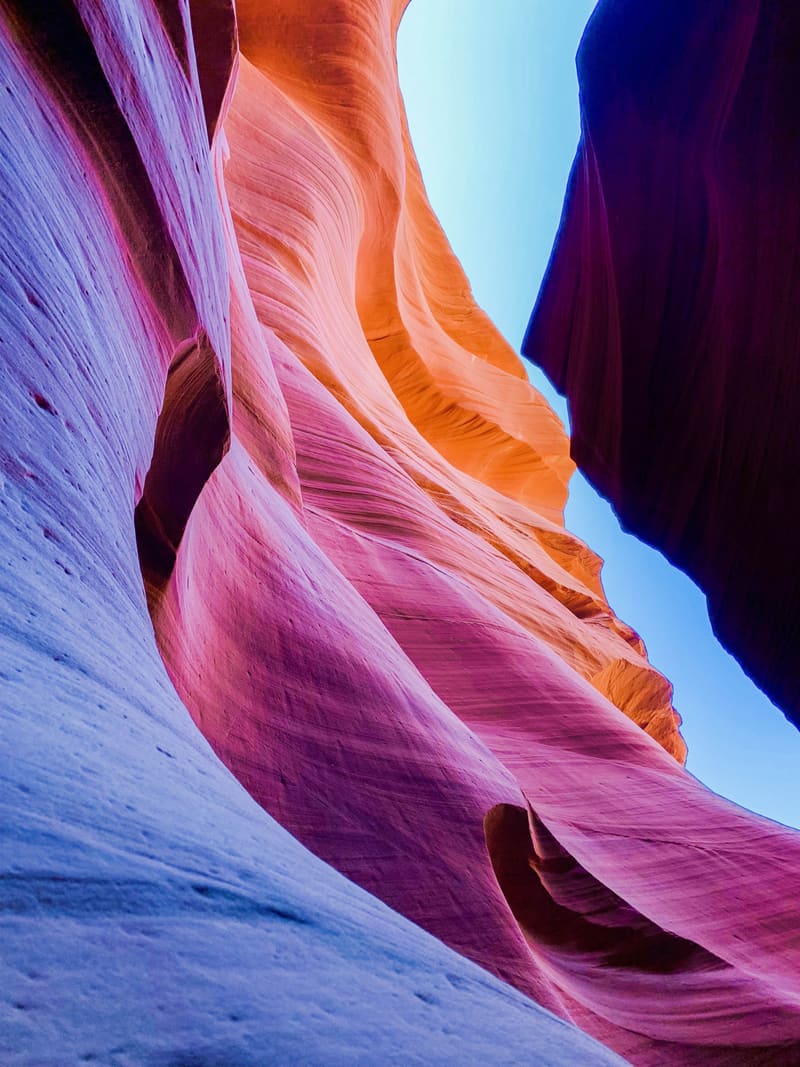 Purple, magenta and orange sandstone walls of Antelope Canyon rising toward a wedge of pale blue sky
