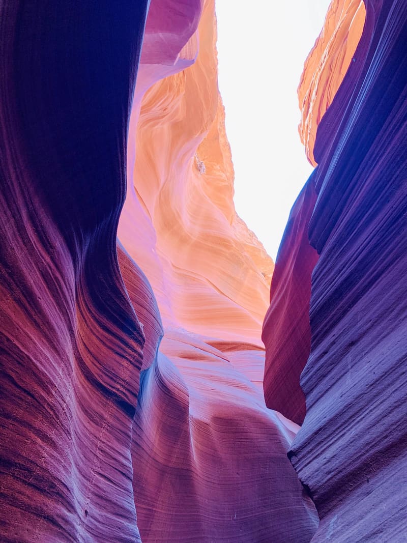 Deep purple slot canyon walls at Antelope Canyon frame a peach-lit sandstone face and a bright white gap of sky overhead