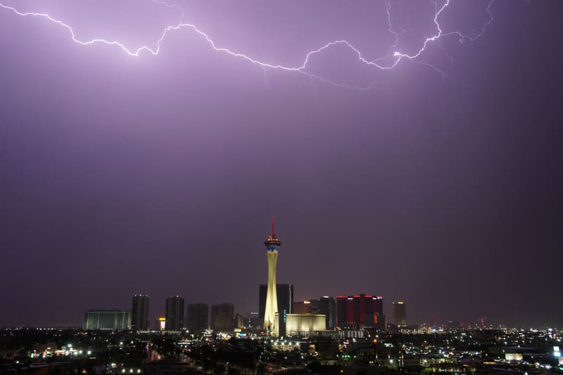 Long lightning bolt crawling across the top of a purple sky over the Strat tower and Las Vegas skyline at night