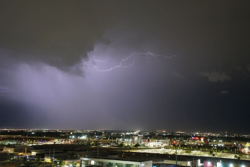 Branching crawler lightning fans out beneath a dark storm cloud above the lights of the Las Vegas valley at night