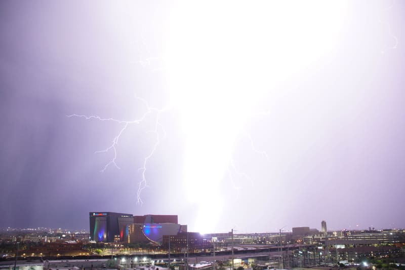 Blown-out column of lightning with thin branching filaments across a pale sky above the World Market Center, Las Vegas
