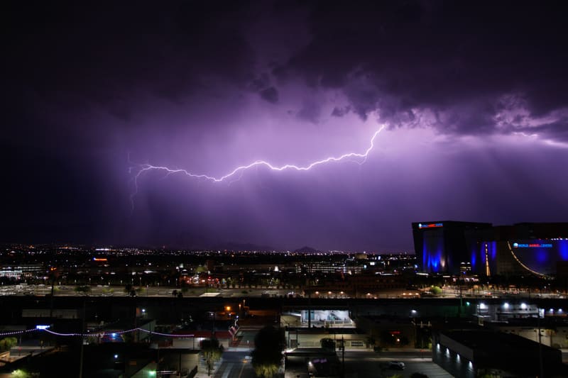 Long horizontal lightning bolt crawls across a purple storm sky over Las Vegas, desert mountains and city lights below
