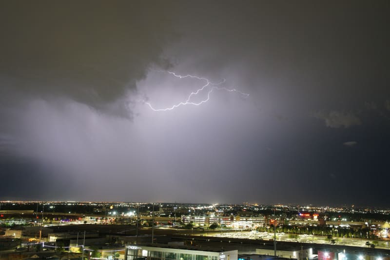 Horizontal cloud-to-cloud lightning crawls across a purple storm sky above the lit sprawl of Las Vegas at night