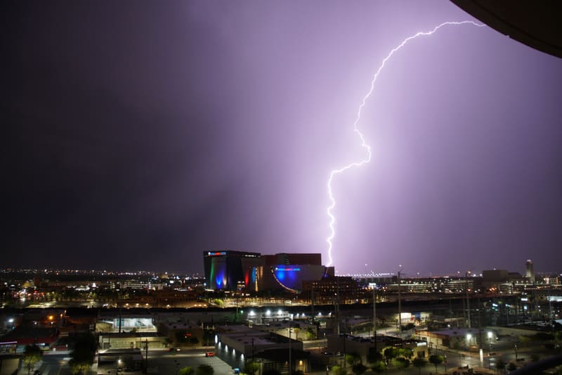 Curving lightning bolt arcs down from a purple sky and strikes behind the World Market Center in downtown Las Vegas