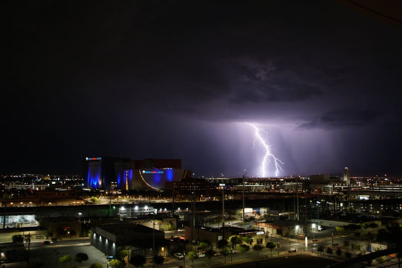 Forked lightning bolt splits in two as it strikes beyond Las Vegas, purple storm sky over the blue-lit World Market Center