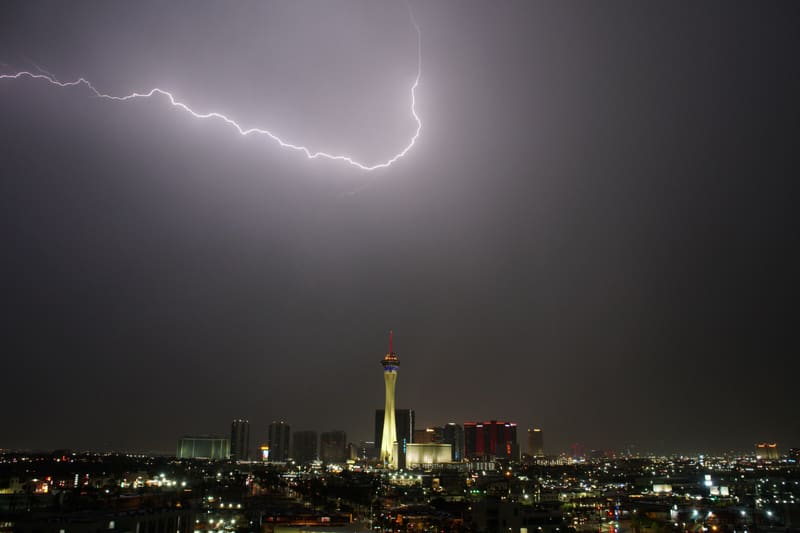 Horizontal lightning bolt hooking across a dark gray sky high above the Strat tower and the lit Las Vegas skyline