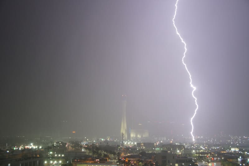 Thick lightning bolt striking the ground to the right of the Strat tower through rain haze over Las Vegas at night