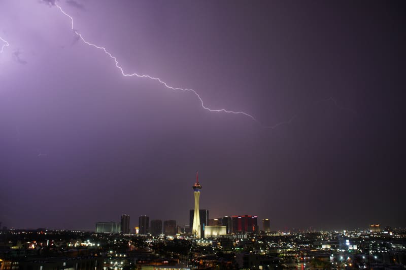 Long lightning bolt crawls diagonally across a purple night sky above the Strat tower and Las Vegas city lights
