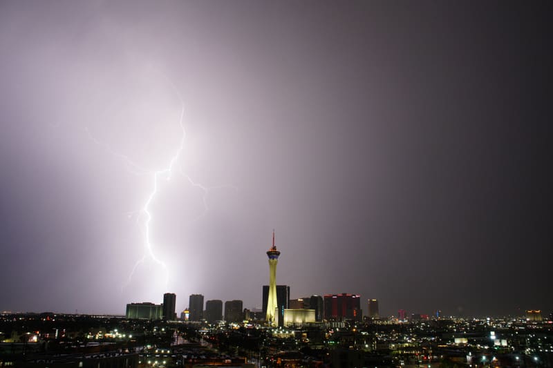 Bright lightning bolt with spidery side branches bleaching a lavender sky over Las Vegas, the Strat tower lit gold at center