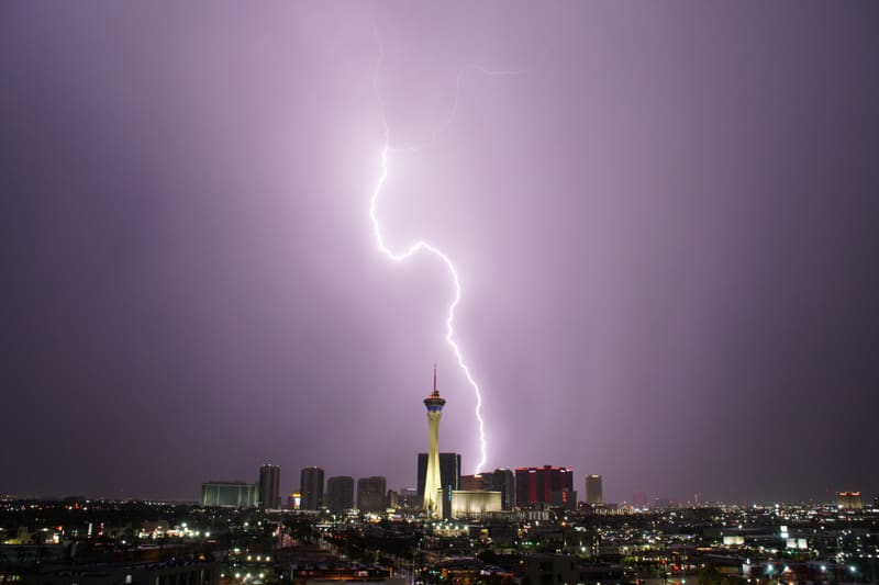 Forked lightning bolt curving down through a lavender night sky to strike beside the Strat tower in Las Vegas