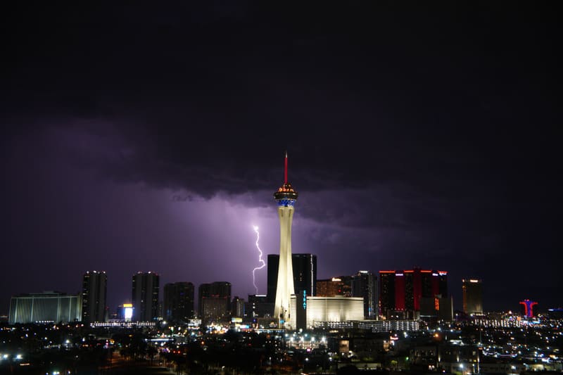 Thin lightning bolt strikes down just left of the Strat tower on the Las Vegas skyline under a purple storm sky