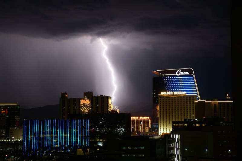 Lightning bolt strikes behind downtown Las Vegas casinos, the Circa and Golden Nugget signs lit under a dark storm cloud