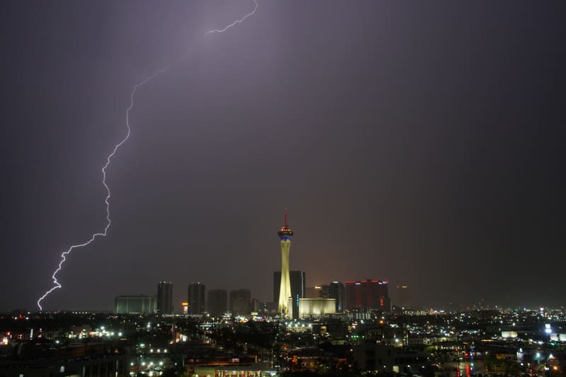 Jagged lightning bolt touches down at the far left of the Las Vegas skyline, the Strat tower lit under dark clouds