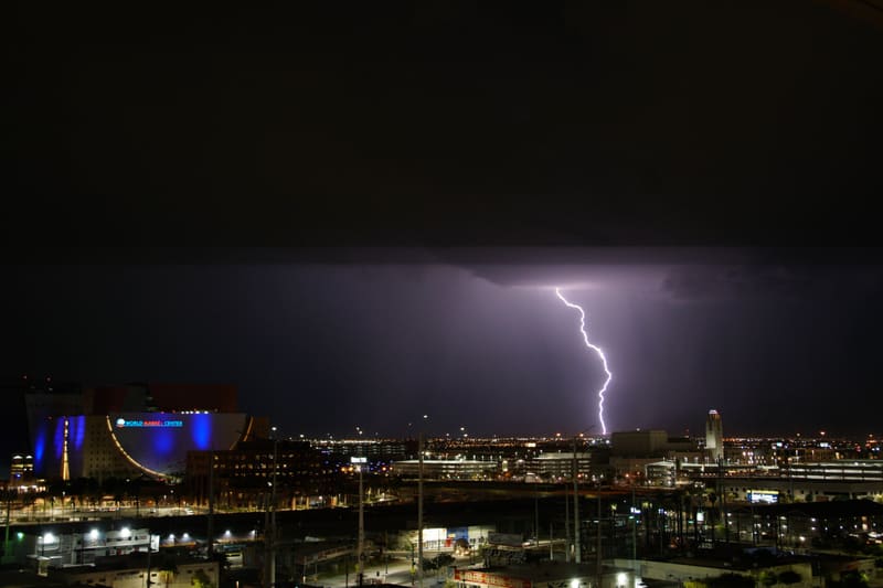 Lone lightning bolt drops from a heavy cloud deck to the horizon, far right of the blue-lit World Market Center in Las Vegas
