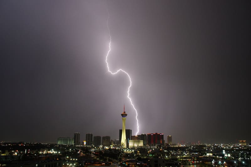 S-shaped lightning bolt snaking down from a lavender sky to strike just right of the glowing Strat tower in Las Vegas