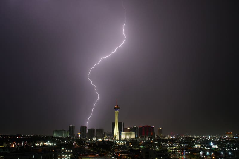 Single jagged lightning bolt dropping from a dark purple sky to the skyline left of the Strat tower in Las Vegas
