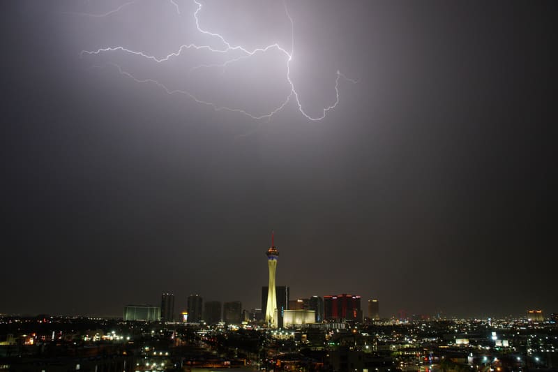 Spidery cloud-to-cloud lightning branching across a dark sky above the Strat tower and Las Vegas city lights