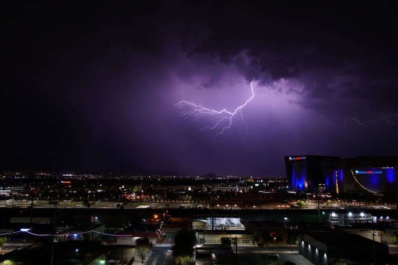 Spidery cloud-to-cloud lightning branches across a violet night sky over Las Vegas, World Market Center lit blue at right