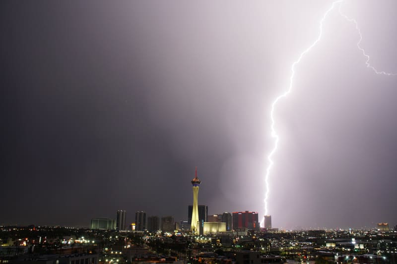 Lightning bolt forking at the top right of a lavender sky and striking behind a red-lit tower next to the Strat in Las Vegas