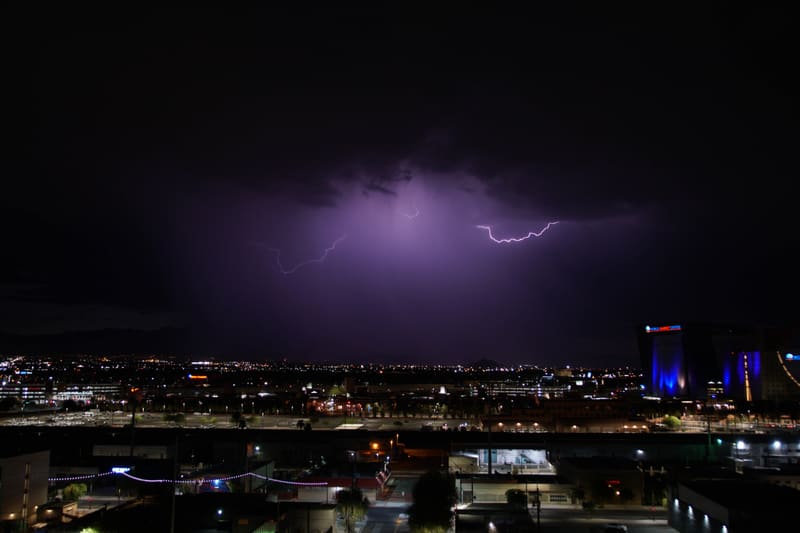 Three small lightning flashes hang in the clouds over Las Vegas, purple glow in a dark monsoon night sky, city lights below