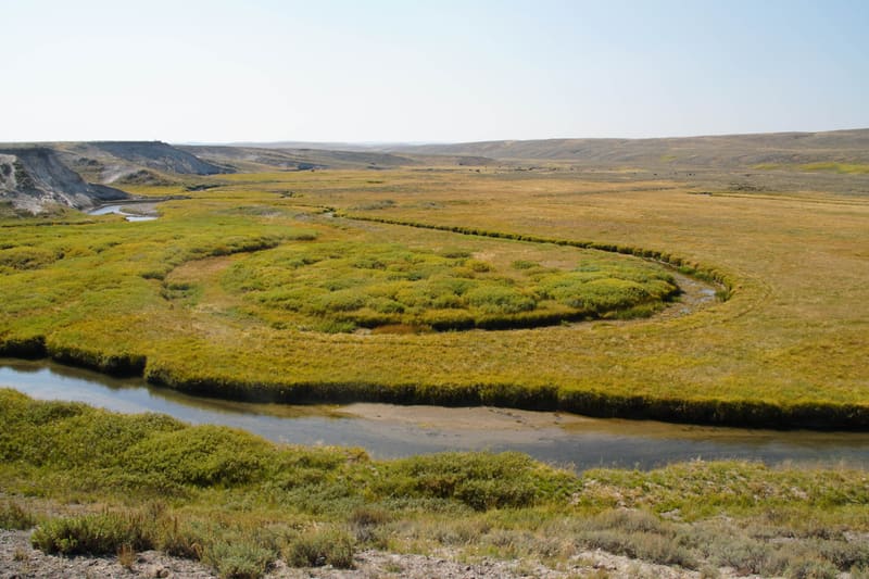 River looping almost fully around a patch of green grass in a wide golden valley, low bluffs on the hazy horizon